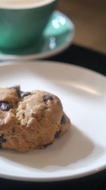 Lezzetli bir çikolatalı kurabiye sıcak bir içeceğin yanındaki tabakta duruyor..