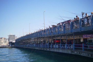 İnsanlar açık mavi gökyüzünün altında İstanbul 'daki canlı bir rıhtımdan balık avlıyor.