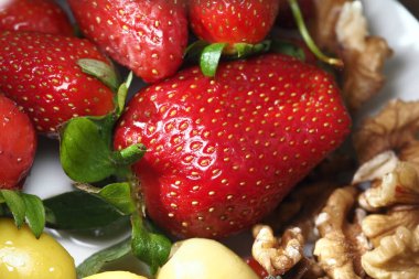 Cevizlerin yanında yeşil yapraklı parlak kırmızı çilekler..