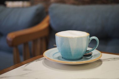 Kapuçino dolu mavi bir fincan kanepenin yanındaki mermer masada oturuyor..