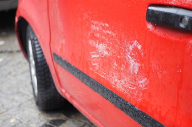 Kırmızı bir arabanın yan tarafında aşınma ve yırtılma izleri var..