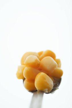 Tatlı mısır taneleri metal bir kaşıkta duruyor, beyaza karşı işaretlenmiş..