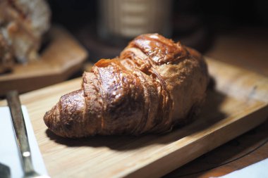 Sıcak bir kruvasan ahşap bir tahtanın üzerinde oturup tadını çıkarmayı bekler..