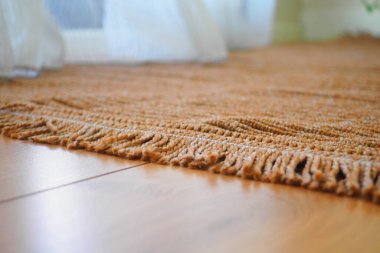 Ahşap bir zeminde örülmüş bir halının yakın plan görüntüsü detaylarını gözler önüne seriyor..