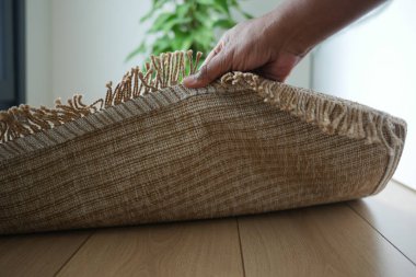 Bir el örülmüş bir halıyı iyi aydınlatılmış bir yaşam alanına sarıyor..