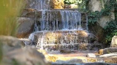 Yeşil taşlarla çevrili sakin bir şelale taşların üzerine dökülür..