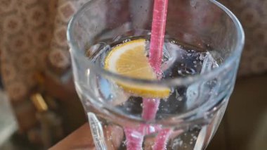 Bir el, limonlu ve pembe pipetli bir bardak köpüklü suyu tutar..