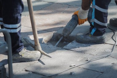 Trafik yakınlarda hareket ederken işçiler kaldırımı tamir etmek için araçlar kullanıyor.
