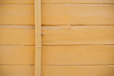 Parlak sarı bir duvar dikey bir boru ve dokulu çizgiler içerir..