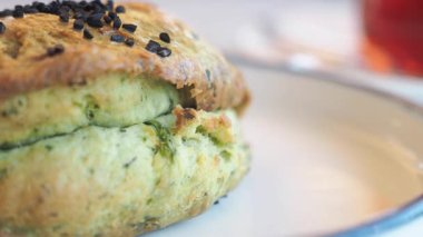 Bir fincan sıcak çayın yanında servis edilen lezzetli yeşil otlu bisküvinin tadını çıkarın..