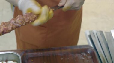 Bir şef, kalabalık bir pazarda eti şiş şiş üzerinde ustalıkla şekillendirir..