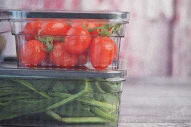 Bright red tomatoes and green spinach in clear containers on wood.