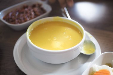 A rich yellow soup is served in a bowl beside a dish of beans.