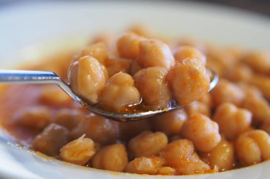 Chickpeas cooked in a rich and spicy sauce on a spoon.