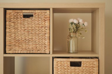 A shelving unit displays woven storage baskets and a flower vase.
