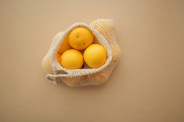 Açık ağ torbası pürüzsüz bir yüzeyde duran parlak limonlar içeriyor..