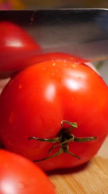 Sıcak bir mutfakta taze domateslerin dikkatlice dilimlenişini izleyin..