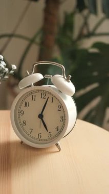 Bitkilerle çevrili ahşap bir masada klasik bir çalar saat..