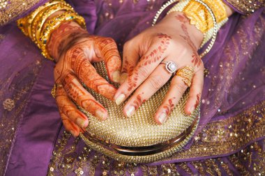 Karmaşık kınalı eller bir şenlik olayında parlak bir altın debriyaj tutuyor..