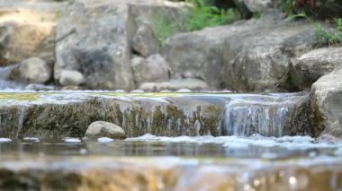 Su yavaşça kayalık yüzeylere dökülür ve huzurlu bir atmosfer yaratır..