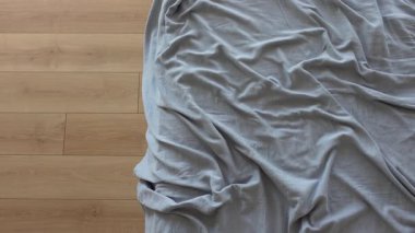 Yumuşak sabah ışığı kırışık gri çarşaflı bir yatakta parlar.