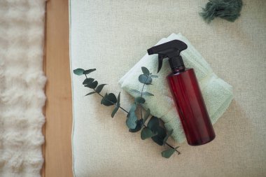 Bir sprey şişesi okaliptüs yapraklarının yanında katlanmış bir havlunun üzerinde duruyor..