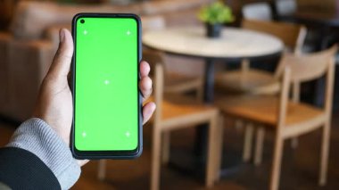 Bir kişi kafede dinlenirken yeşil ekranlı bir akıllı telefon gösterir..