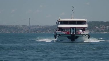 Şehir binaları uzakta yükselirken bir feribot su üzerinde seyahat ediyor..