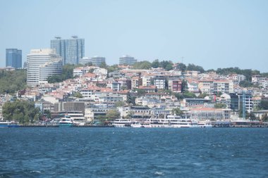 İstanbul şehrinin manzarasında deniz kenarındaki binalar ve tekneler sergileniyor.