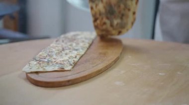 Bir şef yuvarlayarak ve tahta bir tahtanın üzerinde keserek yassı ekmek hazırlar..