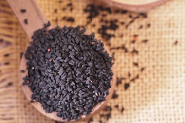 Siyah kimyon tohumu ahşap bir kaşıkta desenli bir yüzeye yığılır..