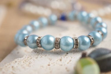 Mavi boncuklar ve gümüş aksanlar tarafsız bir yüzeyde şık bir bilezik oluşturur..