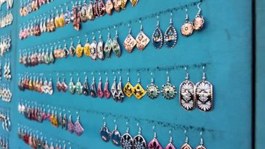 Çeşitli tasarımlardaki eşsiz küpeler parlak mavi bir ekrana asılıyor..