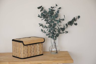 Tahta bir yüzey üzerinde okaliptüs olan bir vazonun yanında örülmüş bir sepet duruyor..