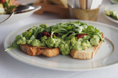 Yeşillik ve domatesli tam tahıllı ekmeğin üzerinde lezzetli bir avokado tostu..