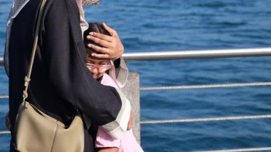 Bir çocuk, su kenarındaki bir ebeveynden sıcak bir sarılma alır..