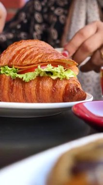 Bir insan kruvasan ve taze sebzeyle yapılmış bir sandviç alır..