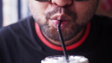 Bir insan kafede pipetle soğuk bir içecek içer..