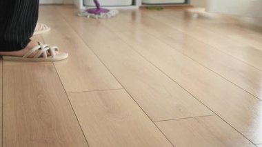 İnsan evde parmak arası terlik giyerken ahşap yerleri temizler..