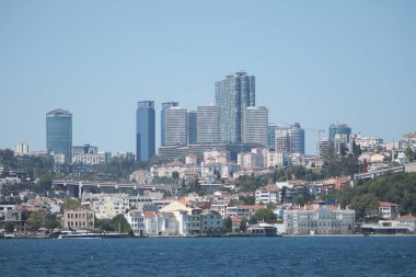 Arka planda açık gökyüzü olan yüksek binalar suyun üzerinde yükselir..