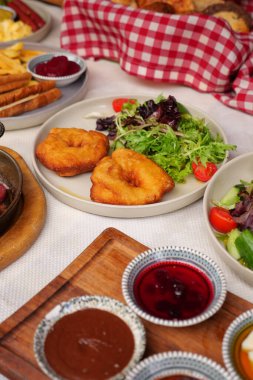 Çeşitli tabaklar masaya konur, salata, ekmek ve sos gösterilir..