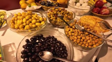 İnsanlar çeşitli zeytin ve meyvelerle dolu kadehlerin etrafında toplanırlar..