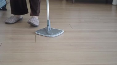 Person mops a wooden floor in a living space during the day.