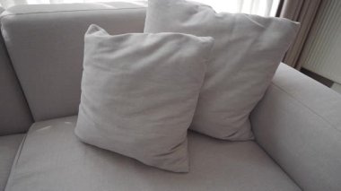 İki yumuşak yastık güneşli bir odada gri bir kanepede dinleniyor..