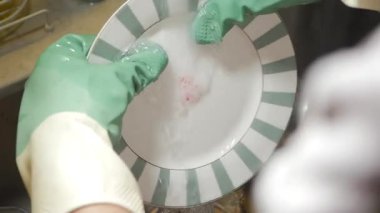 Biri mutfak lavabosunda sabun ve suyla tabak yıkıyor..