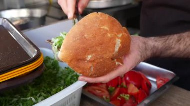 Bir insan taze marul ve sebzelerle sandviç hazırlar..