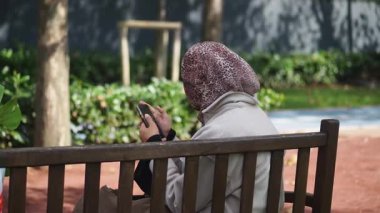 Kadın parkta bir bankta otururken telefonuna bakıyor..