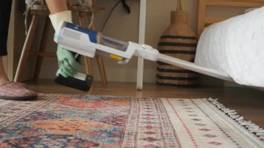 Temizlikçi, yatak odasındaki halıyı temizlemek için elektrikli süpürge kullanıyor..