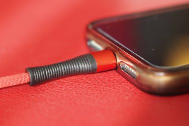 Bir akıllı telefon kırmızı bir yüzeydeki şarj kablosuna bağlanır.