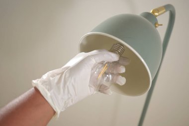 Bir insan beyaz eldiven kullanarak lambanın ampulünü değiştirir..